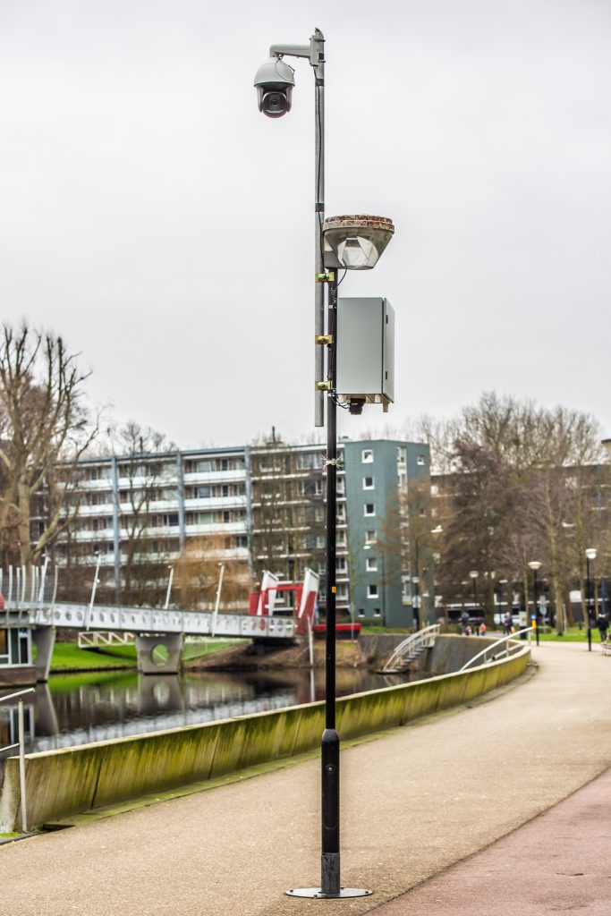 Cameratoezicht op een lichtmast bij een parkpad en woonwijk