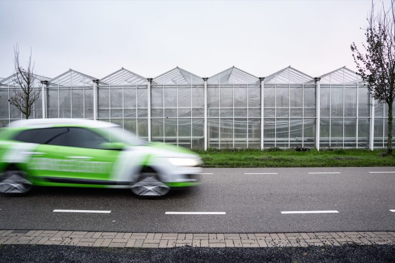 Rijdende surveillancewagen van EW Security met kassen op de achtergrond